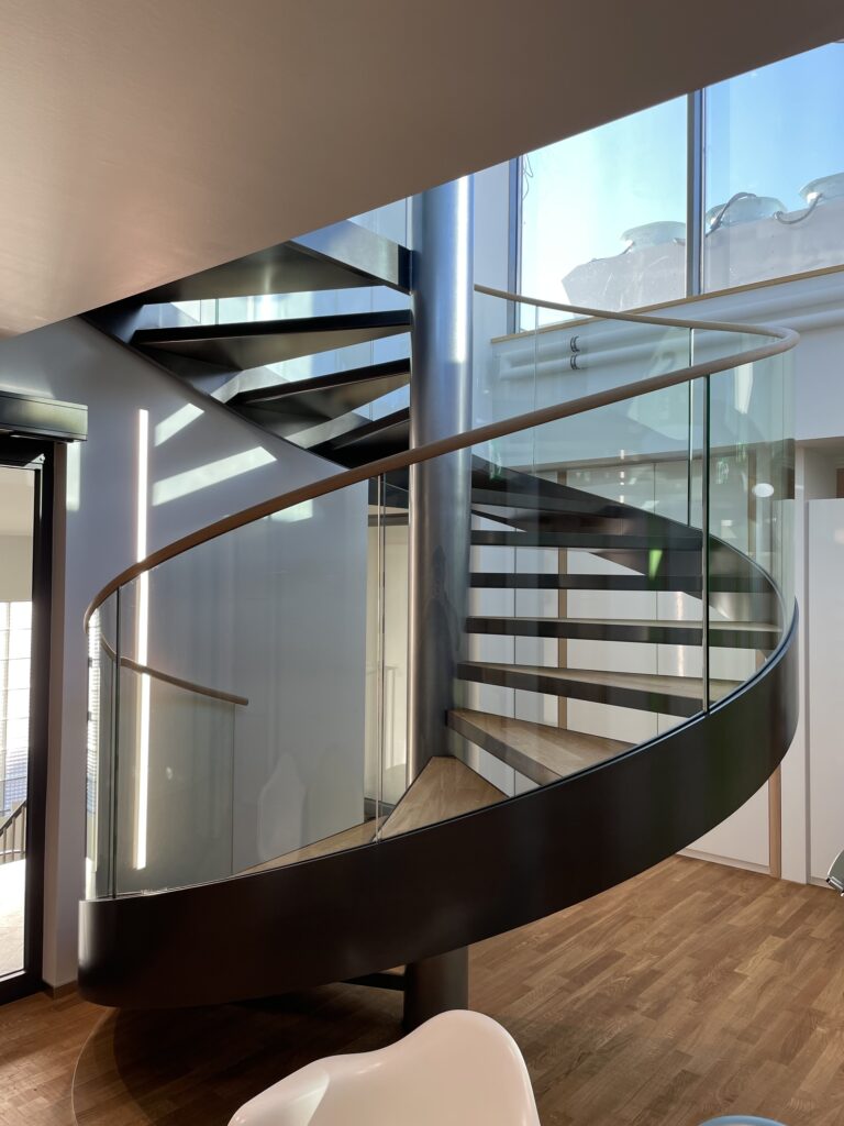 Spindeltreppe aus Stahl mit Glasgeländer und Holztritten