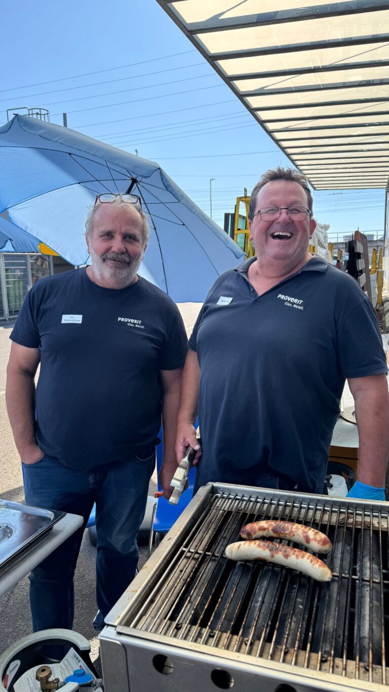 Zwei Proverit-Mitarbeiter lachen am Grill beim Jubiläumsfest